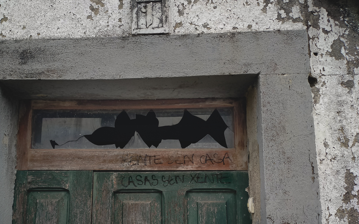 Pintada en la puerta de una casa abandonada, que dice en gallego "Gente sin casa, casas sin gente"